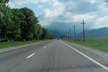Long stretch of highway surrounded by greenery under a cloudy sky in a mountainous region during midday