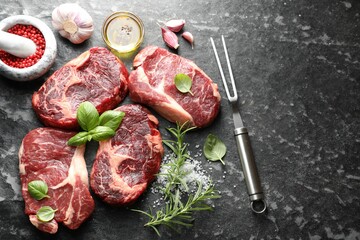 Pieces of raw beef meat, spices and carving fork on dark table, flat lay. Space for text