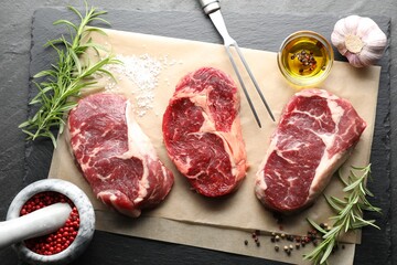 Pieces of raw beef meat, spices and carving fork on black table, flat lay