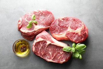 Pieces of raw beef meat and spices on grey table, flat lay