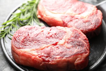 Pieces of raw beef meat and rosemary on dark table, closeup