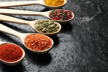 Many different spices in spoons on black table, closeup