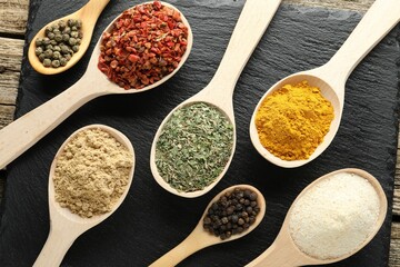 Different aromatic spices in spoons on wooden table, flat lay