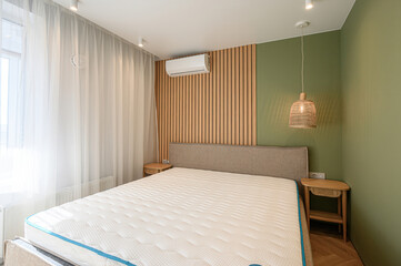 bright bedroom features a large bed, sheer curtains, a wooden slat wall, and a green accent wall. Natural light fills the space