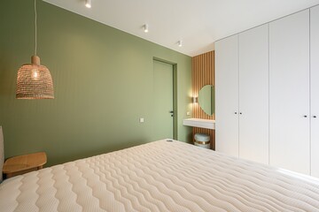 Cozy bedroom with a light green wall, a woven pendant lamp, a white bed, and built-in white...
