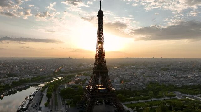 Aerial drone view of the streets of Paris, France, overlooking the famous Eiffel Tower and Champ de Mars at sunrise or sunset. Sun rays pass through the tower. Cinematic 4k. Europe from above