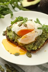 Delicious sandwich with avocado, poached egg, arugula and pumpkin on table, closeup