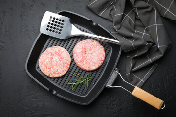 Fresh raw patties for burger and spices in frying pan on black table, top view
