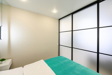 modern room features a bed with turquoise blanket, white sheets, and a frosted glass partition with...