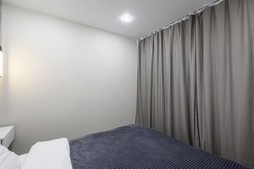 simple bedroom features gray curtains, a bed with a gray blanket and white pillow, and a white wall...