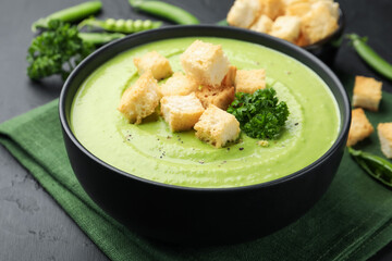 Tasty pea cream soup with croutons and broccoli served on black table, closeup