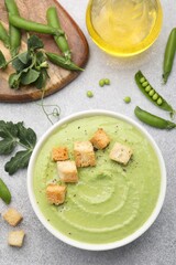 Tasty pea cream soup with croutons served on grey table, flat lay