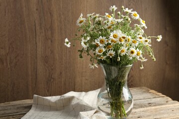 Beautiful chamomile flowers in glass vase on wooden table, space for text