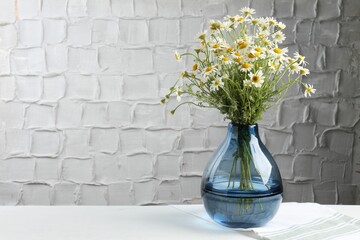 Beautiful chamomile flowers in vase on white table near grey wall, space for text