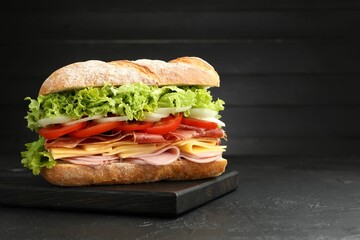 Tasty baguette sandwich with ham and vegetables on black table, closeup. Space for text