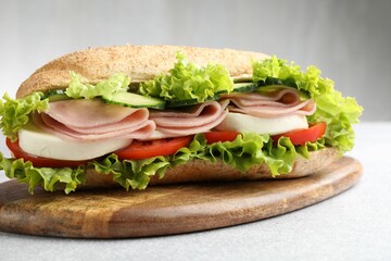Tasty baguette sandwich with ham and vegetables on light grey table, closeup