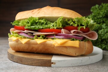 Tasty baguette sandwich with ham, cheese and vegetables on grey textured table against blurred...