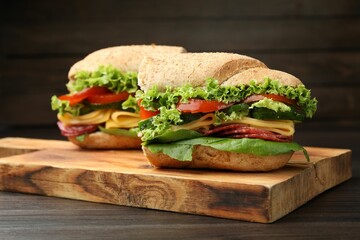 Pieces of tasty baguette sandwich with smoked sausage, cheese and vegetables on wooden table,...