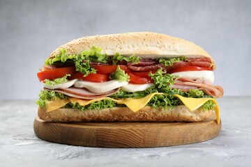 Tasty baguette sandwich with ham, cheese and vegetables on grey textured table, closeup
