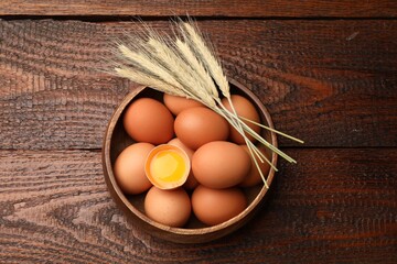 Raw eggs and spikes of wheat on wooden table, top view