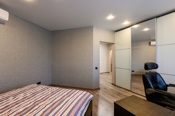 Obraz premium cozy room with a bed, a mirrored wardrobe, and a comfortable chair. It features gray walls, warm lighting, and wooden floors