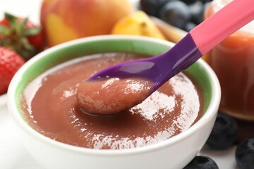 Baby food. Eating tasty puree with spoon at white table, closeup