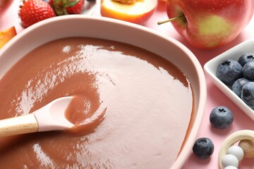 Baby food. Eating tasty puree with spoon at pink table, closeup