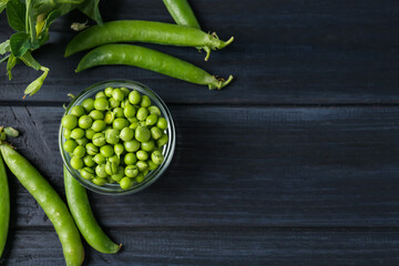 Fresh ripe green peas on black wooden table, flat lay. Space for text