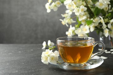 Aromatic jasmine tea and flowers on grey table. Space for text