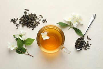 Aromatic jasmine tea in glass cup, flowers and leaves on white table, flat lay