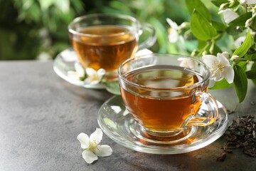Aromatic jasmine tea in glass cups, brew and flowers on grey table outdoors, closeup. Space for text
