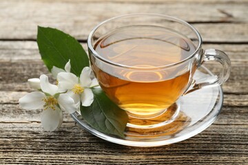 Aromatic jasmine tea in glass cup, flowers and green leaves on wooden table, closeup