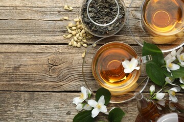 Aromatic jasmine tea in glass cups, teapot, brew and flowers on wooden table, flat lay. Space for text