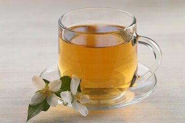 Tasty jasmine tea in cup and flowers at white wooden table, closeup