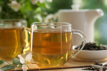 Tasty jasmine tea in cups, teapot, dry leaves and flowers at white wooden table, closeup