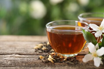 Tasty jasmine tea in cups, dry leaves and flowers on wooden table, closeup. Space for text