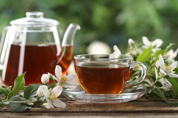Tasty jasmine tea in cup, teapot and flowers on wooden table, closeup