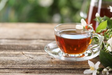 Tasty jasmine tea in cup and flowers on wooden table, closeup. Space for text
