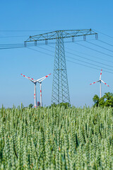 Beautiful wheat farm landscape with wind turbines to produce green energy and high voltage power line towers in wheat field, Germany, Summer, on a sunny day and blue sky.