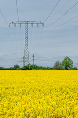 Beautiful farm landscape with yellow rapeseed at blossom field and high voltage power lines in Germany, at Spring and dramatic rainy sky.
