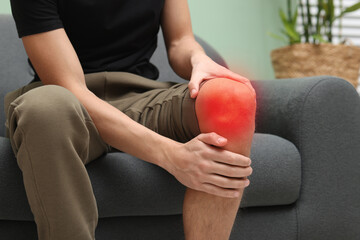 Man suffering from pain in knee on sofa at home, closeup