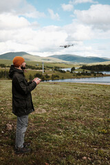 Man flying a drone above Ribnicko Lake in Zlatibor, Serbia. A scenic spring day with hills and water in the background. Travel blogger making video outdoor . Side view portrait.