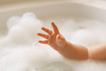 Fototapeta premium Small hand reaches out playfully towards bubbles in bath filled with foam, capturing moment of joy and curiosity. soft texture of bubbles adds to playful atmosphere