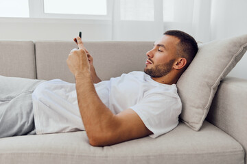 Relaxed man engaging with smartphone at home, reflecting on digital detox and emotional well-being...