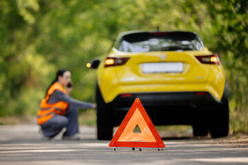 A woman near a broken down car. Orange vest. Road traffic accident. Traveling by car.