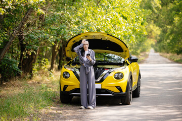 A young woman stands by her car, feeling confused and anxious, and calls for help on the phone. The...