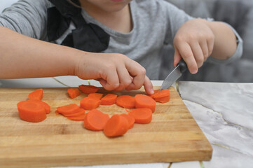 Wooden cutting board covered with orange carrot slices shows child's culinary progress. Detail shot...