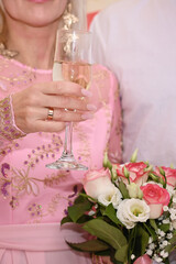 vertical photo Bride in white dress holds champagne glass and fresh flower bouquet during wedding toast. Sparkling wine bubbles. Elegant happy bride with champagne flute and romantic bouquet.