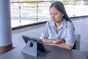 Young Asian woman working on tablet with stylus, focused and productive in a modern indoor/outdoor setting. Ideal for themes of remote work, technology, and casual business