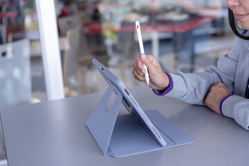 Smiling Asian woman engages with her tablet using a stylus, showcasing productivity and focused work in a bright, modern indoor-outdoor environment, perfect for themes of technology and learning
